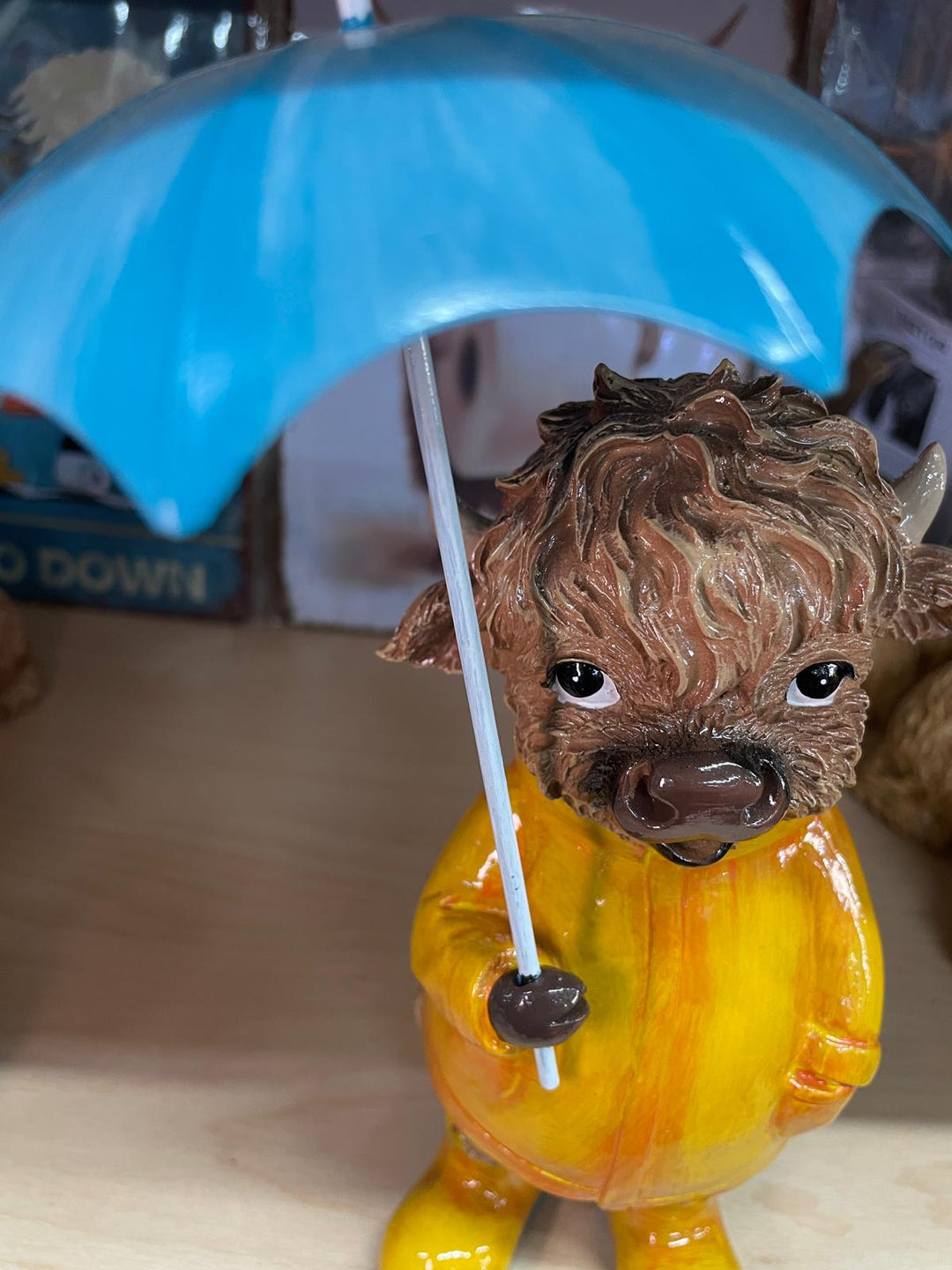 Highland cow in the rain with a blue umbrella yellow rain coat decor ornament