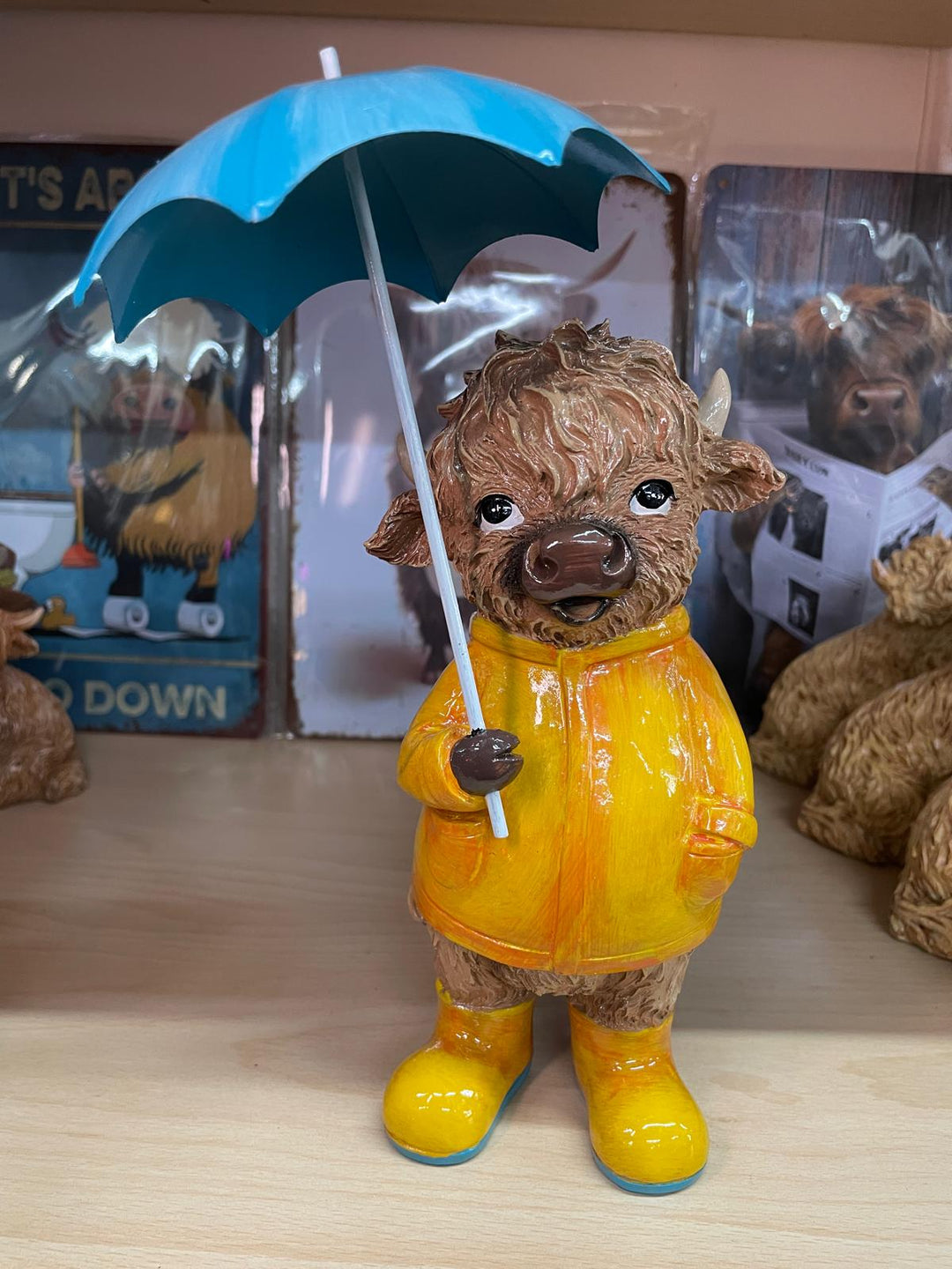 Highland cow in the rain with a blue umbrella yellow rain coat decor ornament
